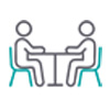 A simple line‑art illustration of two people sitting across from each other at a table, with the text ‘Sharing our Space’ written below in teal.